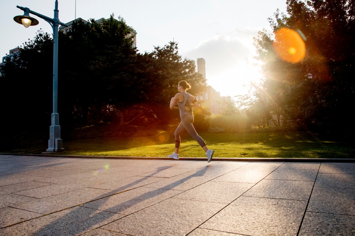 Young active woman running in city park in morning light