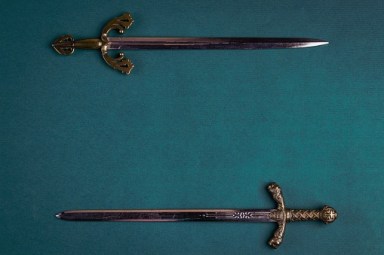 Two old knightly swords on a green velvet background.