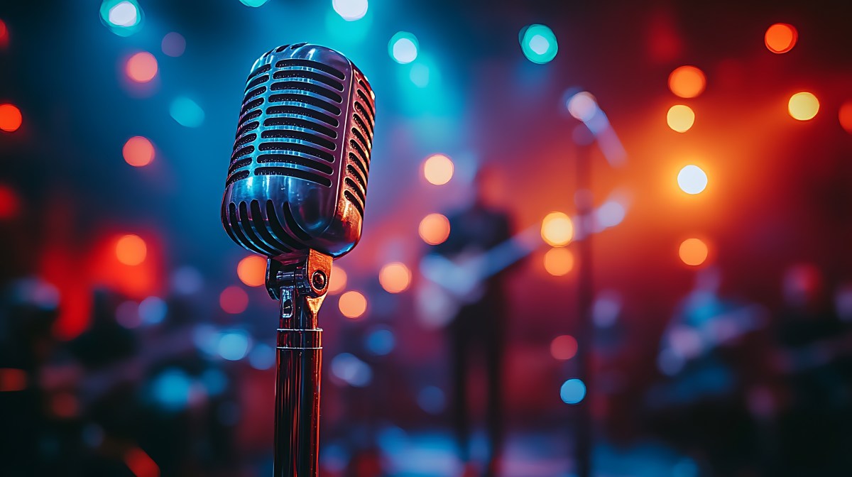 A vintage microphone on stage with a band in the background, lit with colorful stage lights.