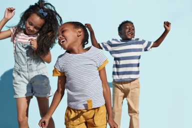 Portrait of kids hanging out & playing together on blue backdrop in sunlight